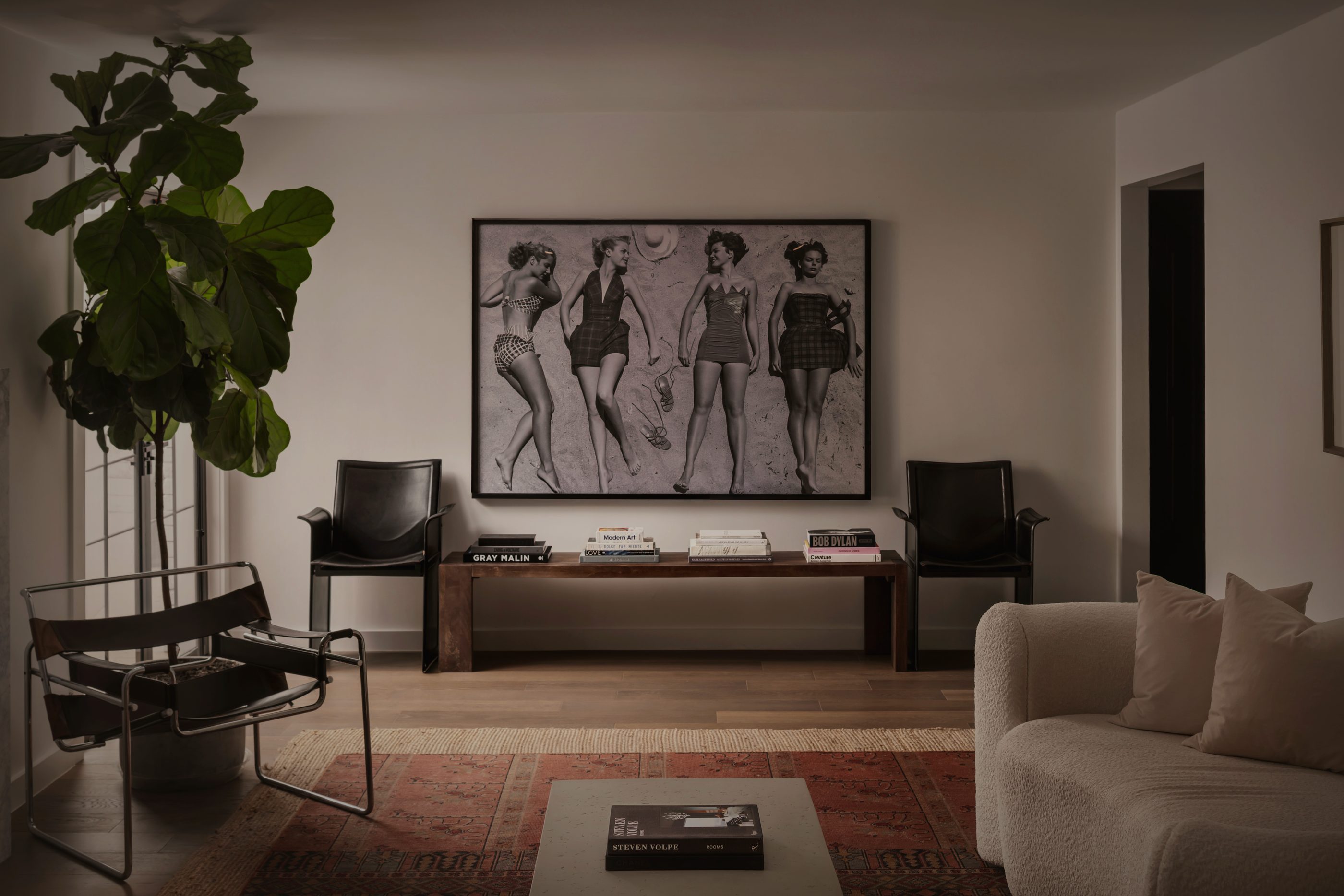 Sitting room with a large framed black-and-white beach photograph above a walnut bench, flanked by black leather chairs