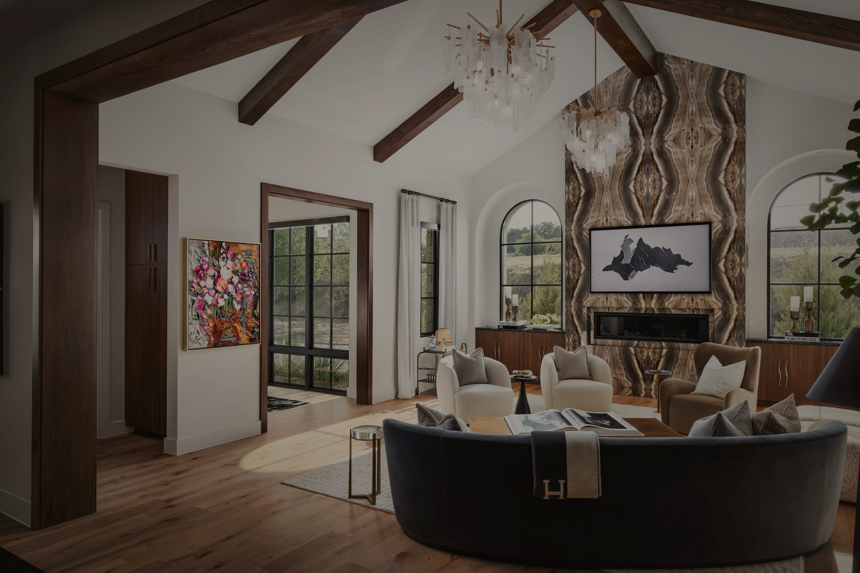 Vaulted living room with dark timber beams, a book-matched stone fireplace wall and a curved navy sofa