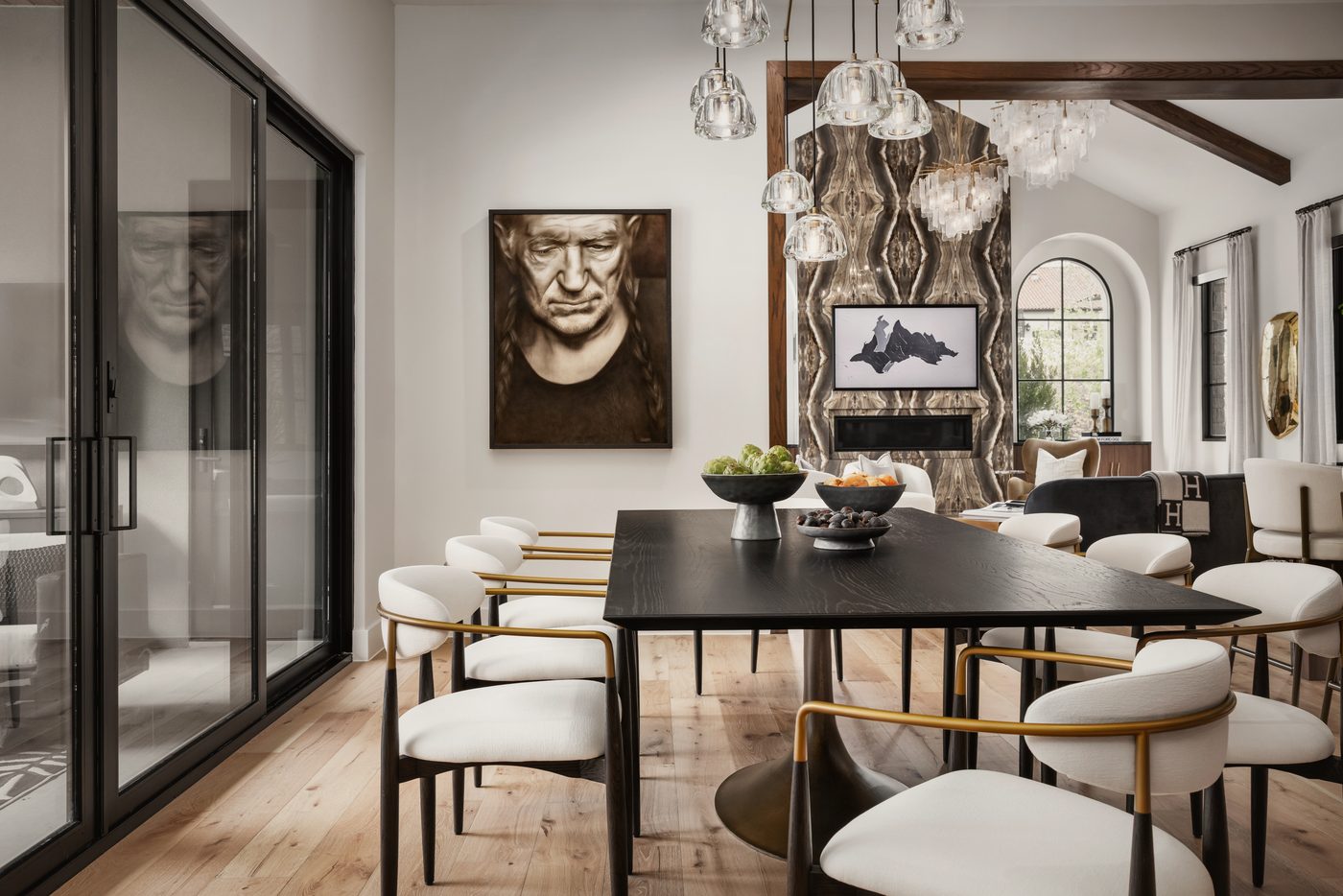 Dining room with a black table, white and brass chairs, glass pendants and a large portrait of Willie Nelson