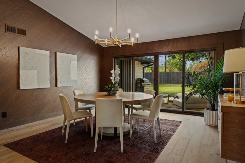 Dining room with a dark wood wall, a brass chandelier over a round table and sliding doors to the yard